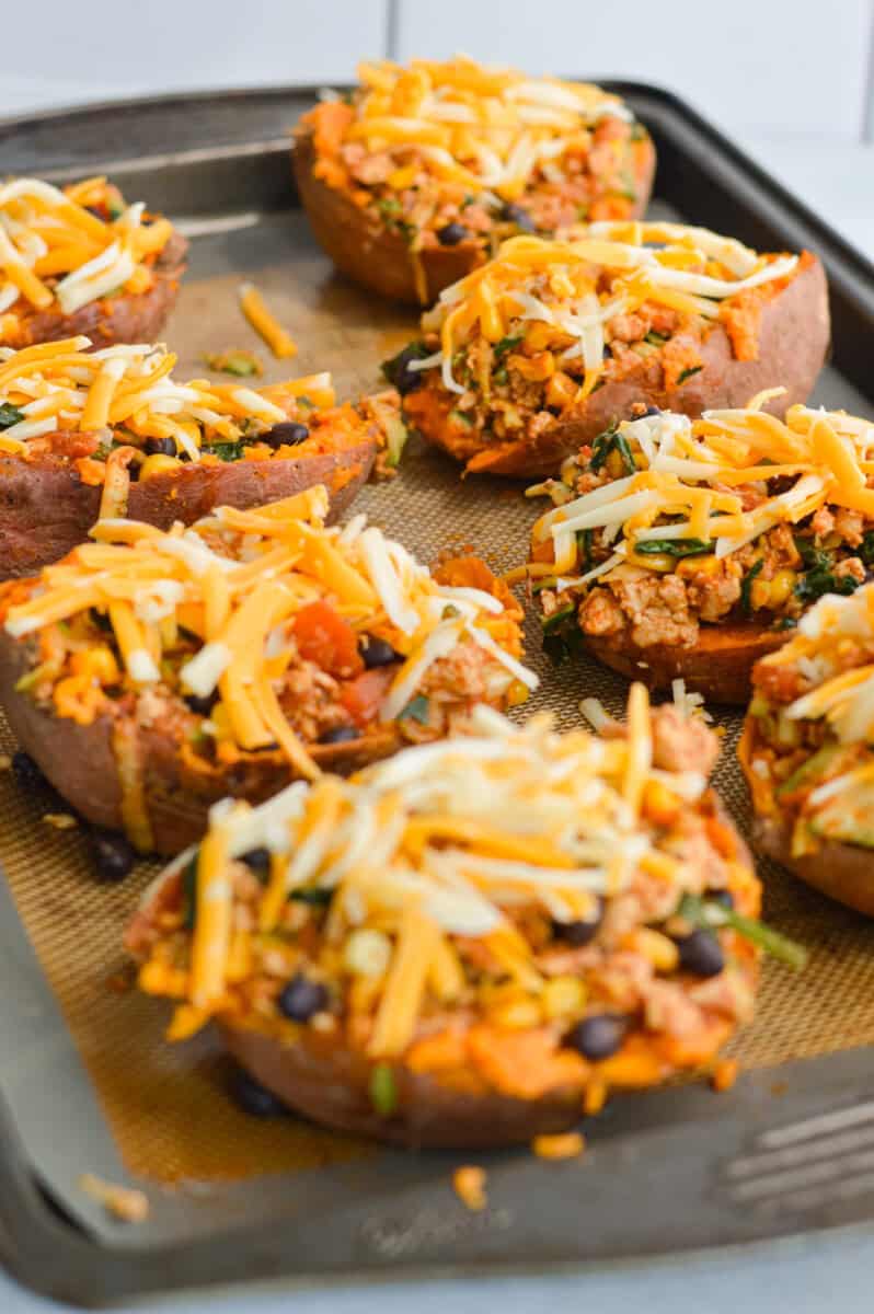 Topping stuffed sweet potatoes with shredded cheese.