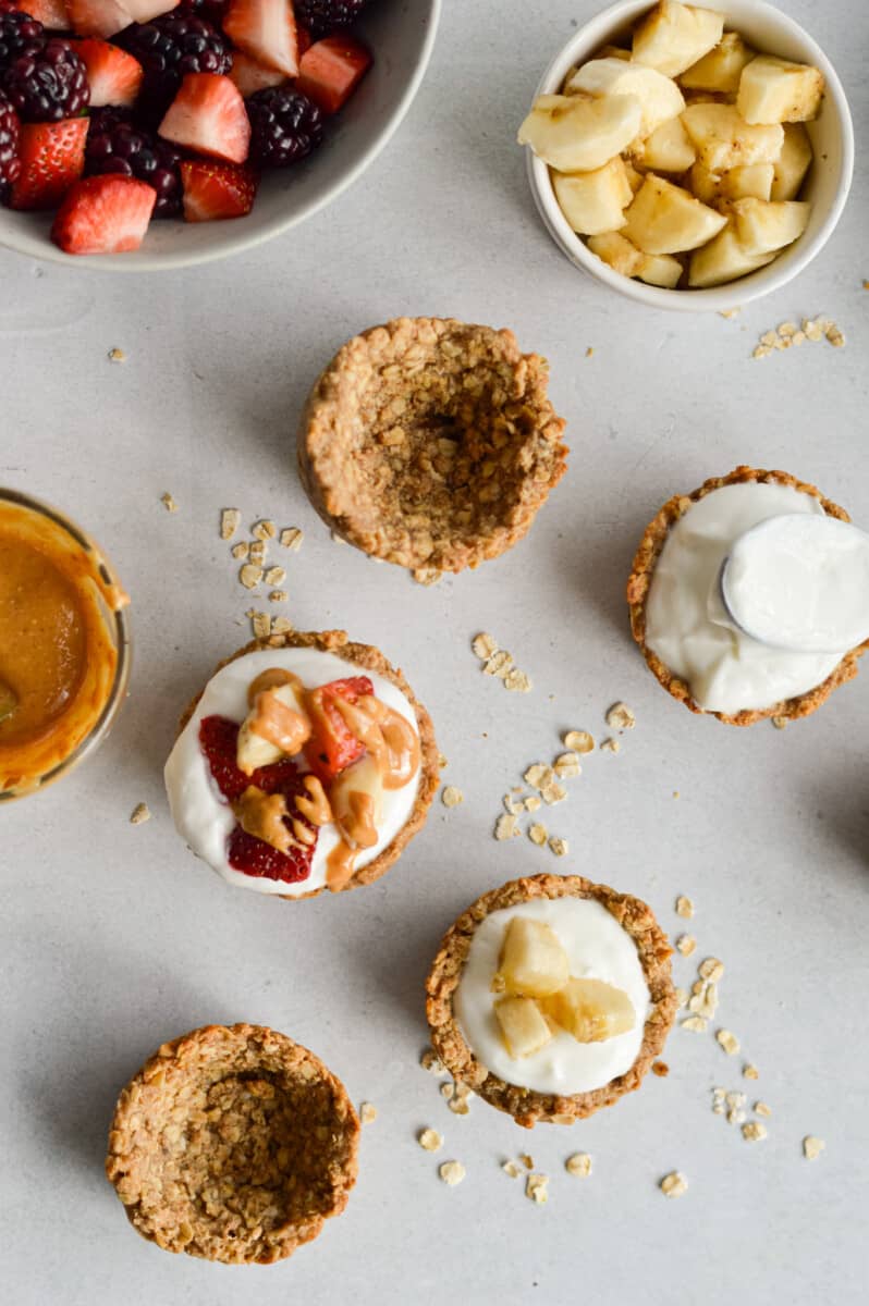 Birds eye of granola cups filled with yogurt and bowls of toppings like banana, berries and peanut butter.