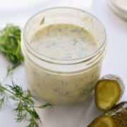 Jar of dill pickle salad dressing next to sprigs of dill and a pickle.