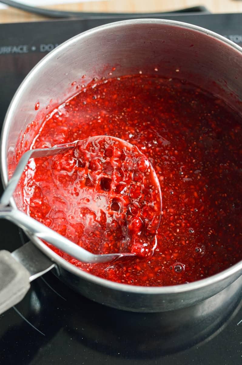 Simmering raspberries and mashing with a potato masher.