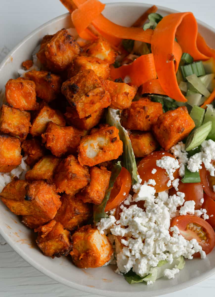 Buffalo tofu in a bowl with veggies and feta.