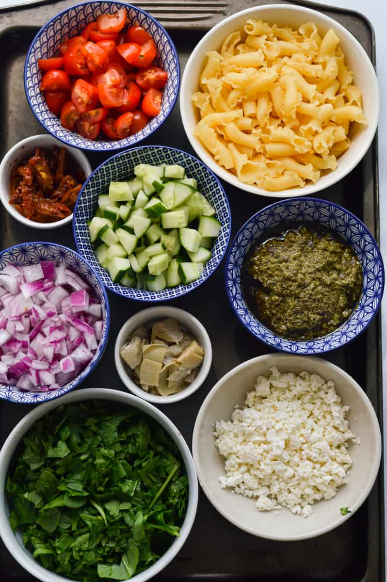 Ingredients including pesto, cut up veggies, feta cheese, and pasta.