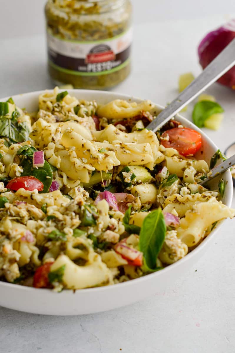Eating pasta salad with a jar of pesto in the background.