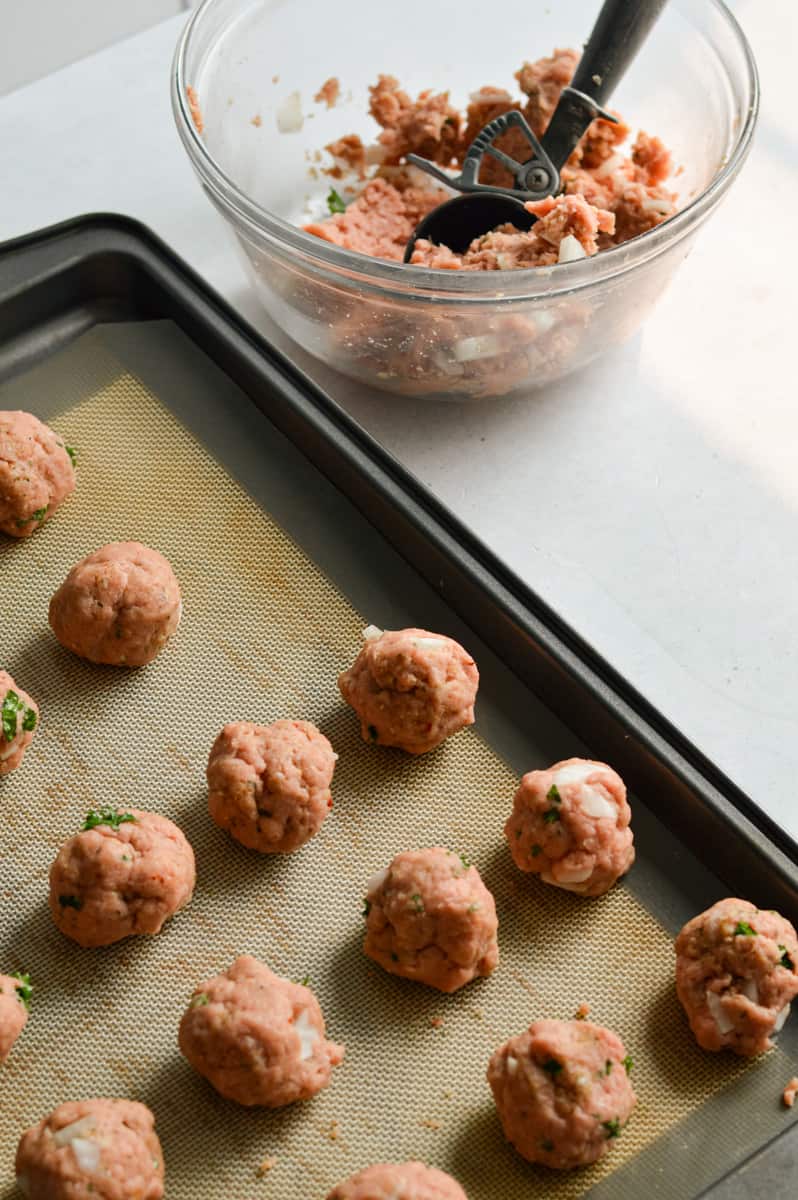 Rolling turkey feta meatballs onto a tray.