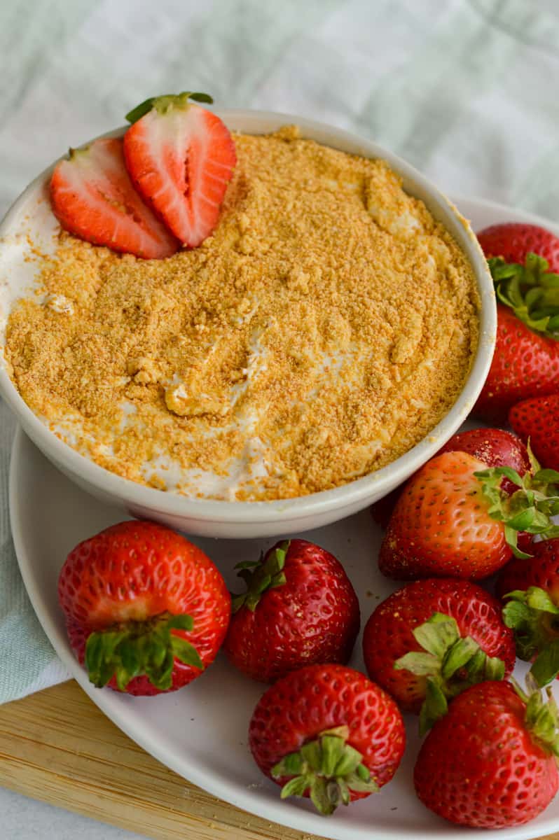 Serving fruit cheesecake dip with a plate of strawberries.