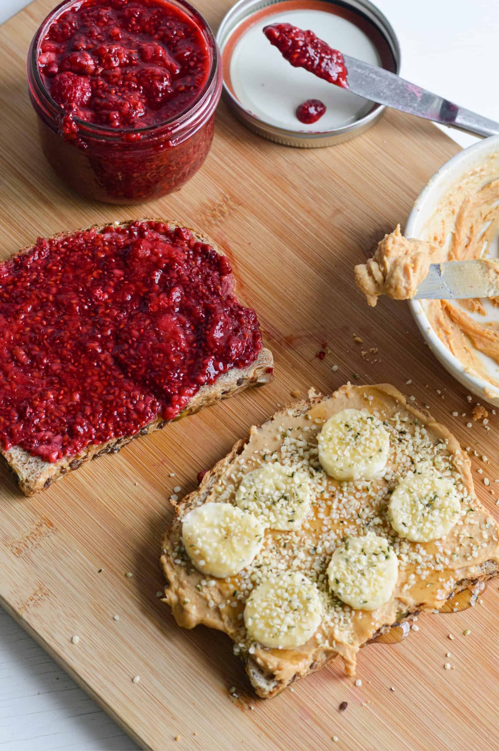Two pieces of toast; one with raspberry chia jam and the other with peanut butter, honey, banana and hemp hearts.