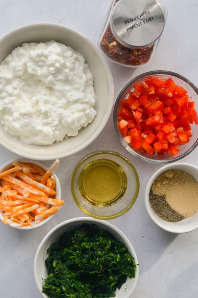 Ingredients including cottage cheese, diced red bell pepper, shredded cheese, olive oil, seasoning, and frozen spinach.