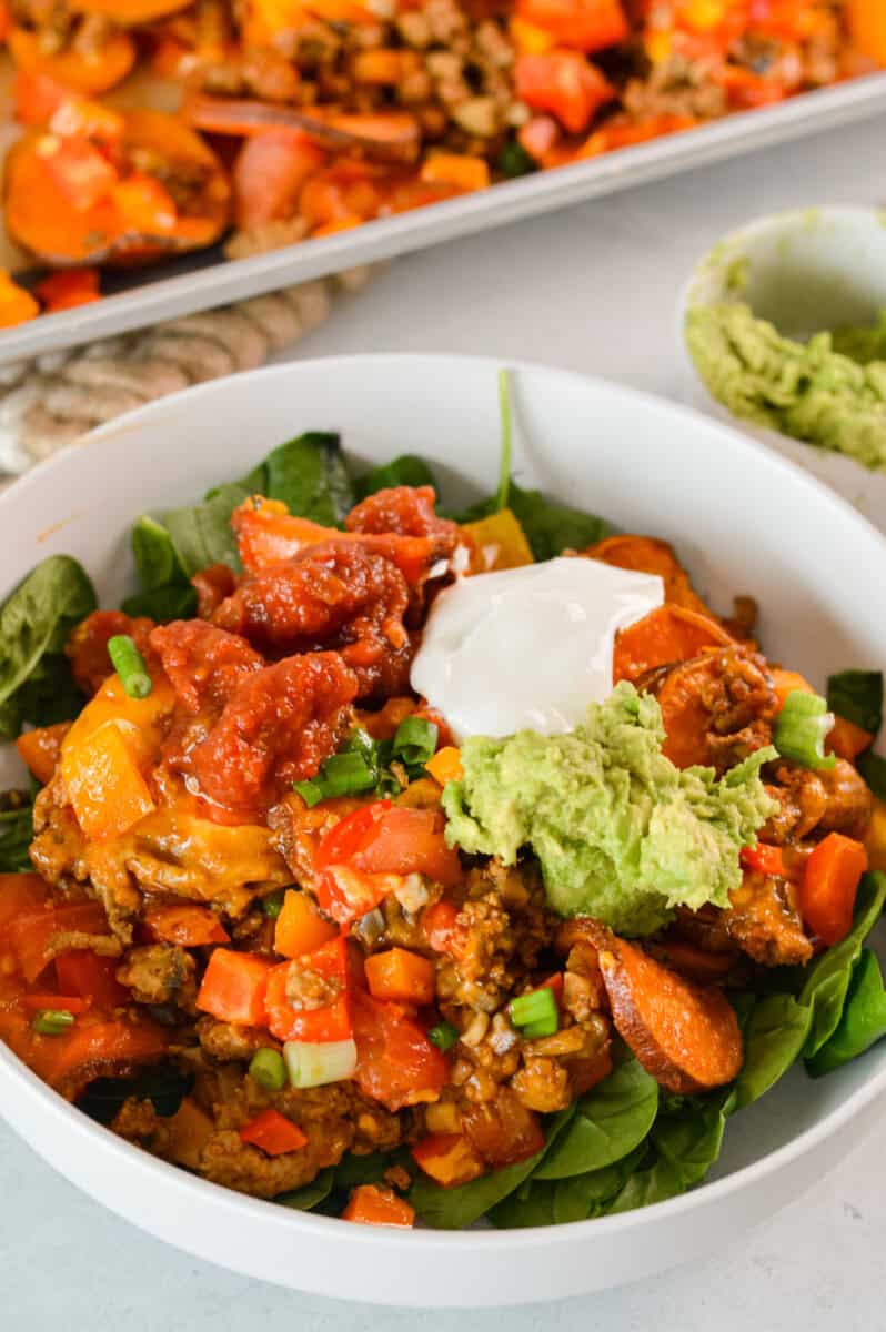 Plate of sweet potato nachos served on a bed of greens, with salsa, greek yogurt and guacamole. 