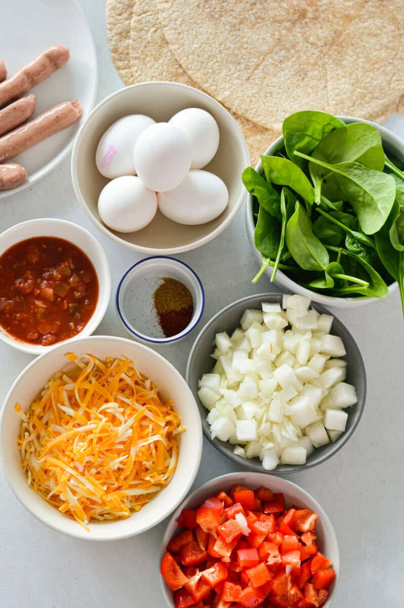 Ingredients including whole wheat tortillas, eggs, spinach, cheese, salsa, spices, onions, red peppers and sausage.