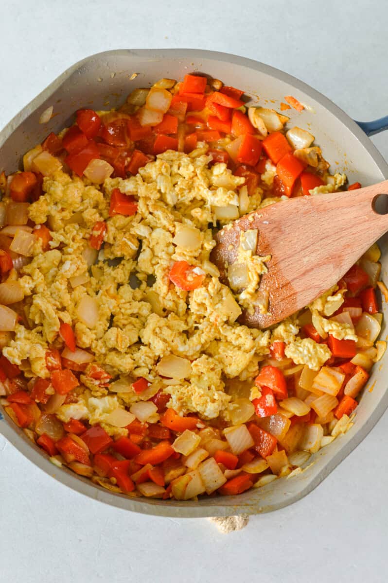 Cooking eggs and veggies together in a pan.
