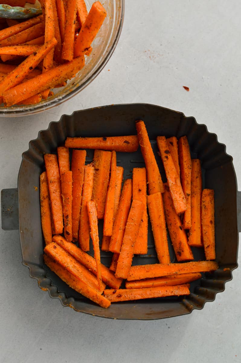 Arranging carrot fries in air fryer basket.