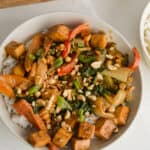 Bowl of satay tofu topped with lime slices and peanuts.