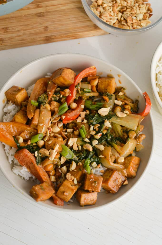 Bowl of satay tofu topped with lime slices and peanuts.