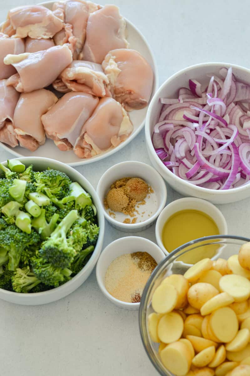 Ingredients including chicken thighs, broccoli, potatoes, red onion, spices, and olive oil.