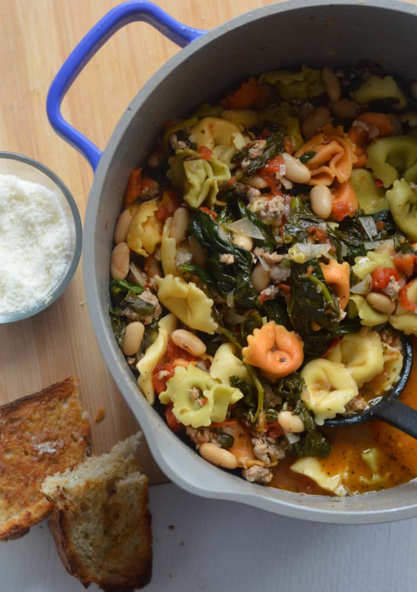 Creamy spinach tortellini soup in a pot, with bread and parmesan on the side.