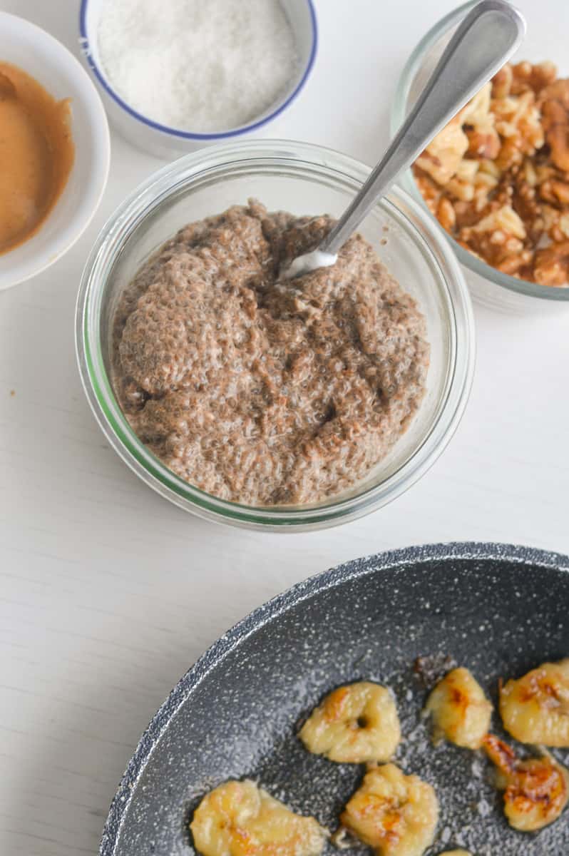 prepared warm chia pudding surrounded by topping options including bananas and walnuts