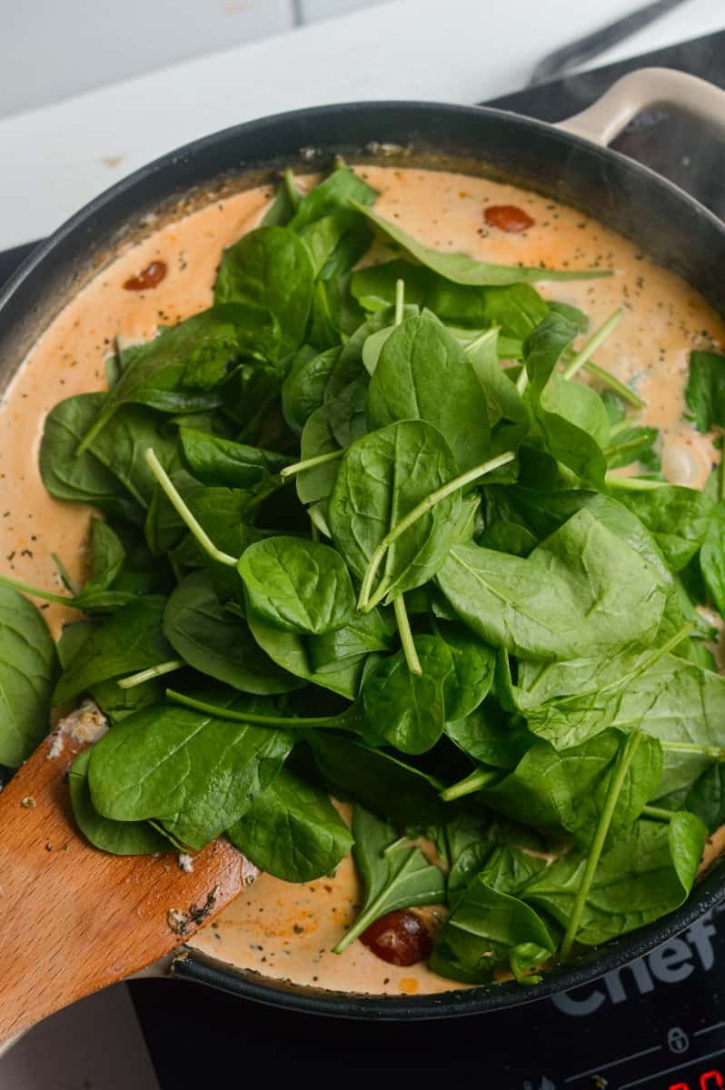 Adding spinach to pasta sauce.