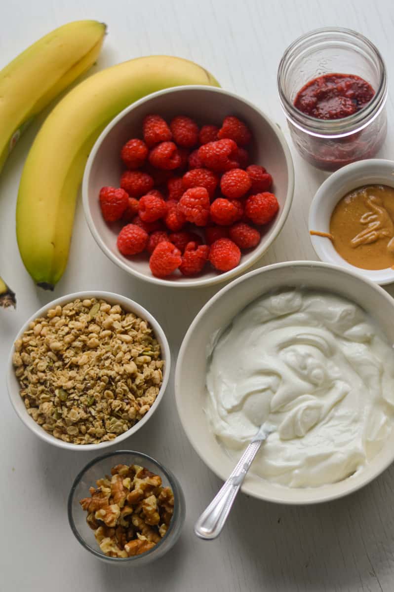Ingredients for Greek yogurt and granola parfaits, including bananas, jam, raspberries and nuts. 