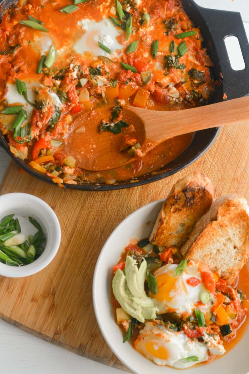 Serving shakshuka in bowls with toast and topping with avocado.