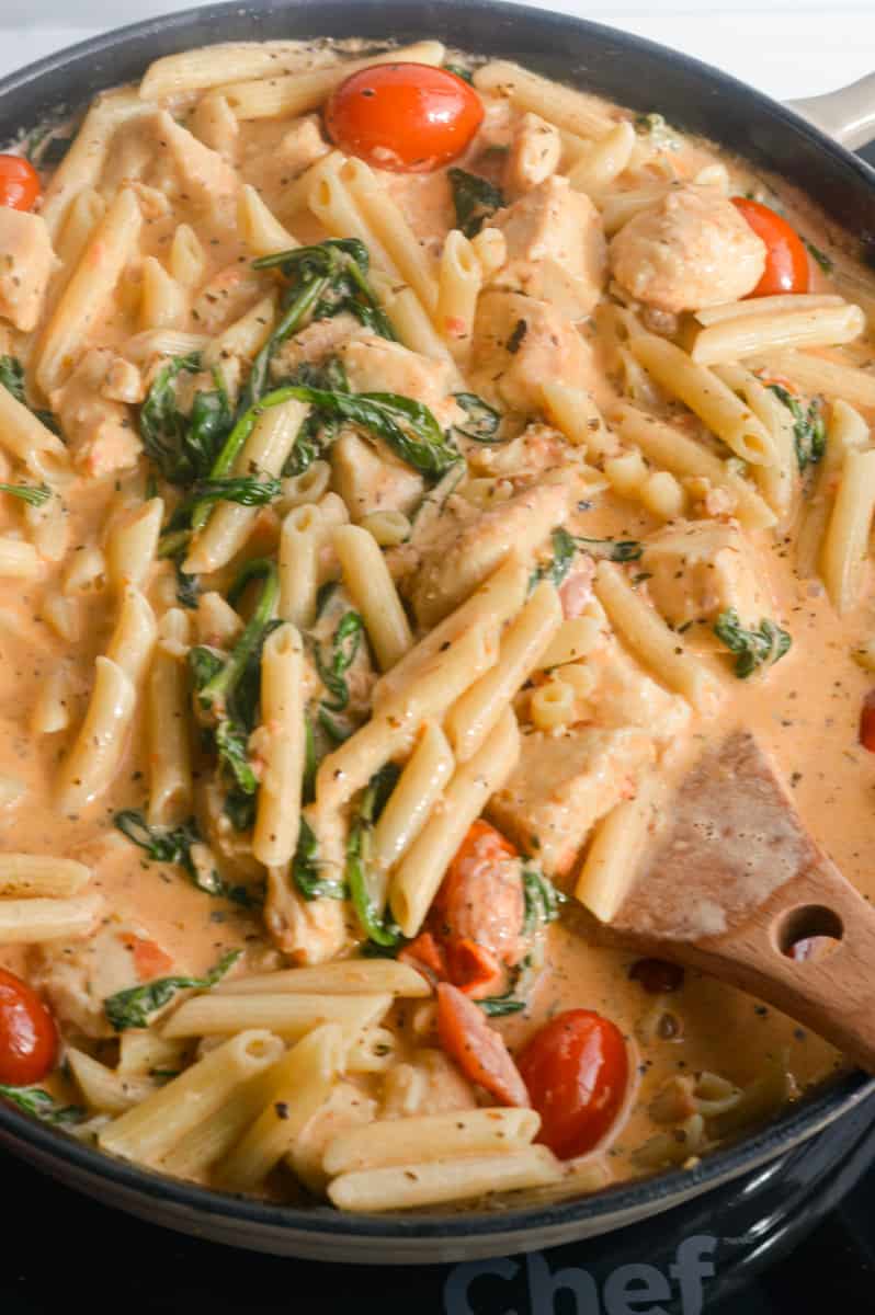 Mixing creamy chicken and tomato pasta.