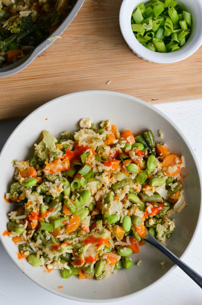 Vegetarian fried rice without soy sauce, topped with green onions and sriracha.