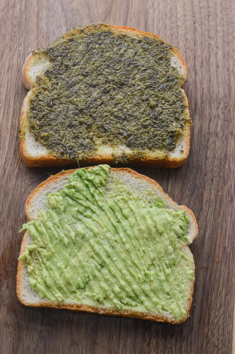 Spreading pesto and avocado on the bread slices.