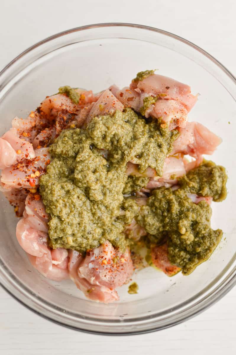 Adding pesto to chicken in a bowl.