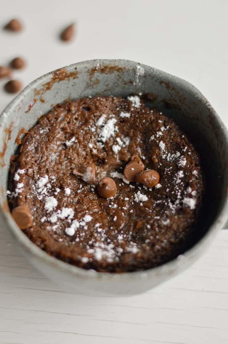 Chocolate protein mug cake topped with chocolate chips and powdered sugar.
