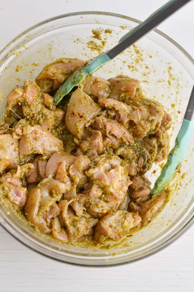 Mixing pesto with chicken in a bowl.