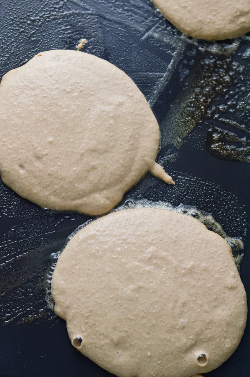 Spooning pancake batter onto a greased griddle.