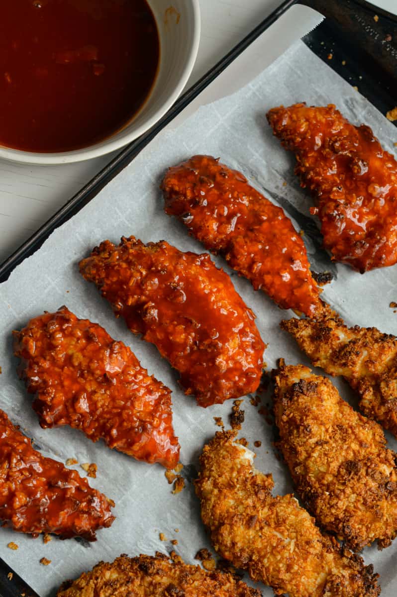 Coating air fryer chicken tenders in buffalo sauce.