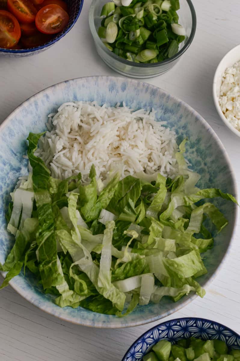 Assembling veggies and toppings in rice bowl.