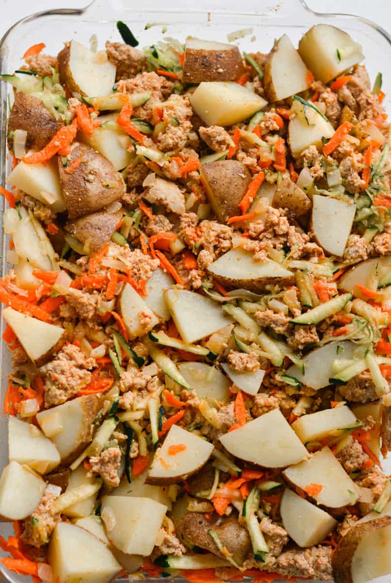 Adding potatoes, ground meat and veggies into casserole tray.