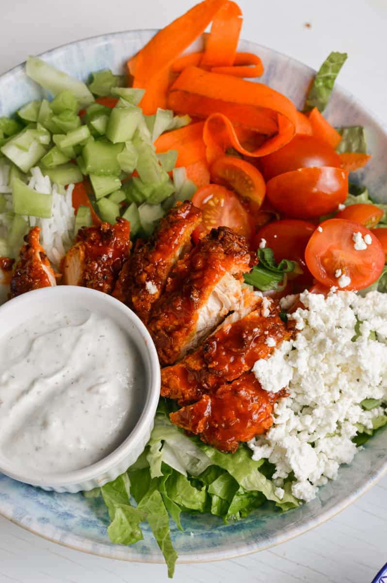 Topping rice bowls with buffalo chicken and serving with ranch dressing.