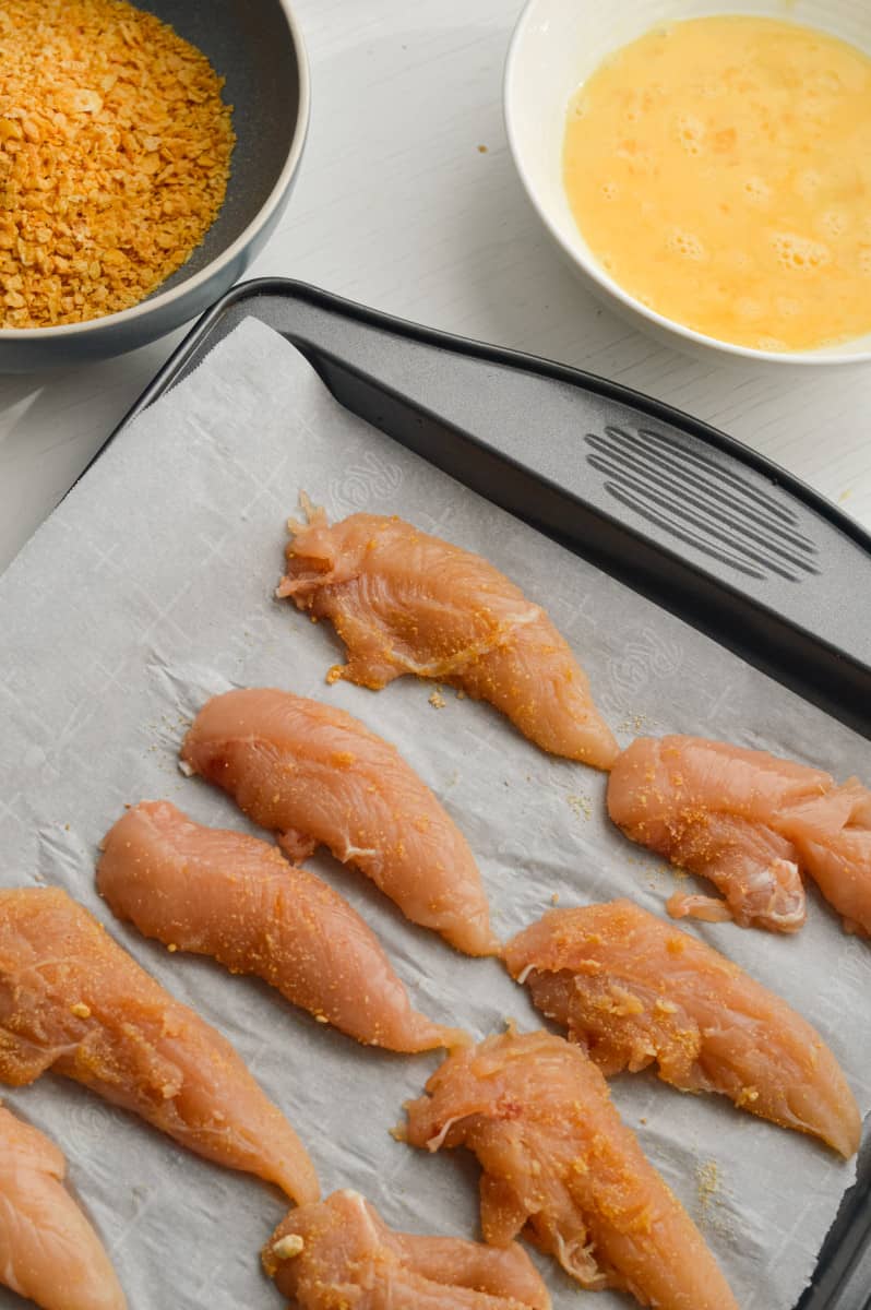 Coating chicken breast in egg and corn flakes.