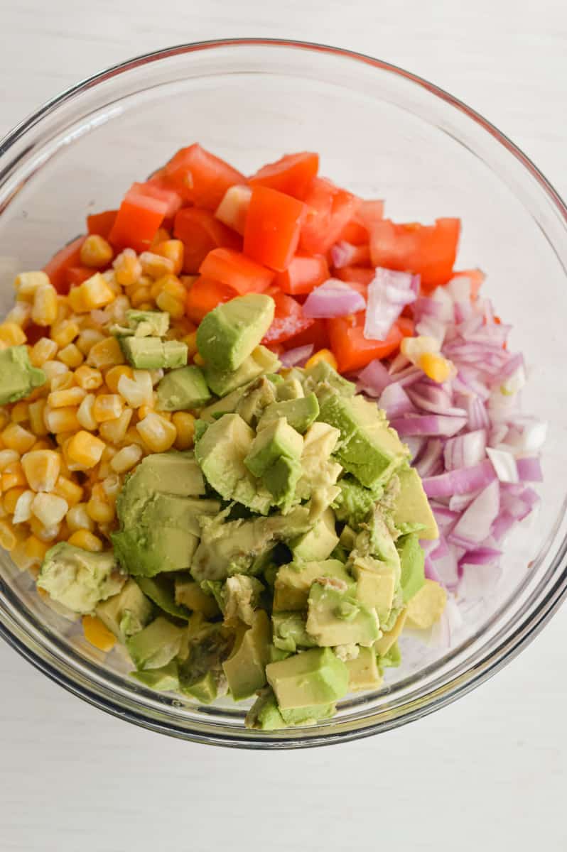 Combining black beans, black eyed peas, avocados, red onions, tomatoes, corn and cilantro in a bowl.