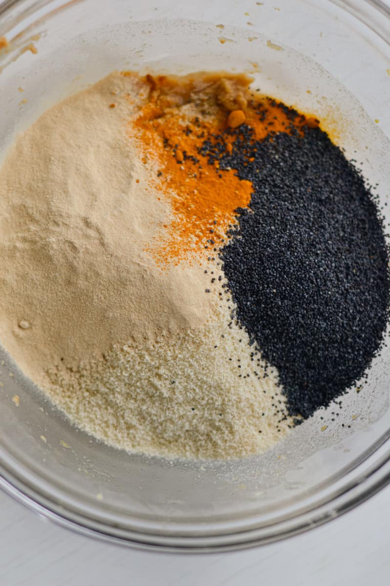 Adding protein powder, almond flour, turmeric and poppyseeds to dough.