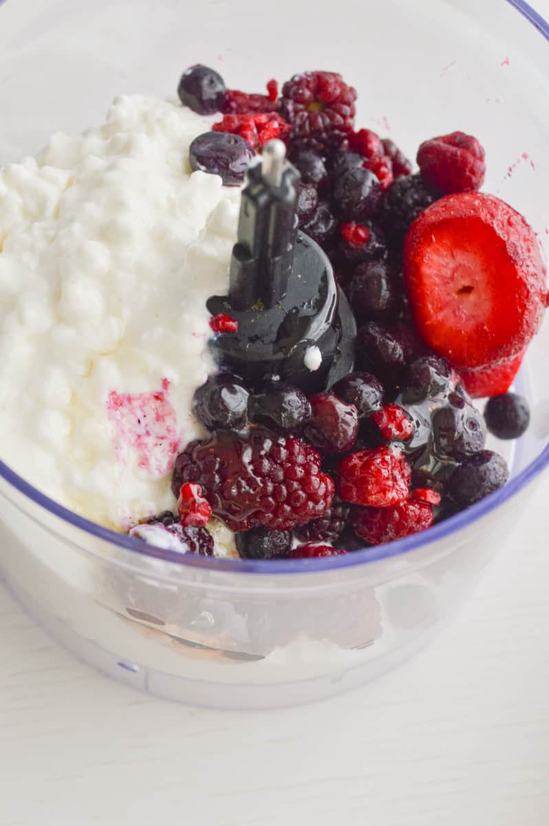 Adding cottage cheese, berries and honey to a food processor.
