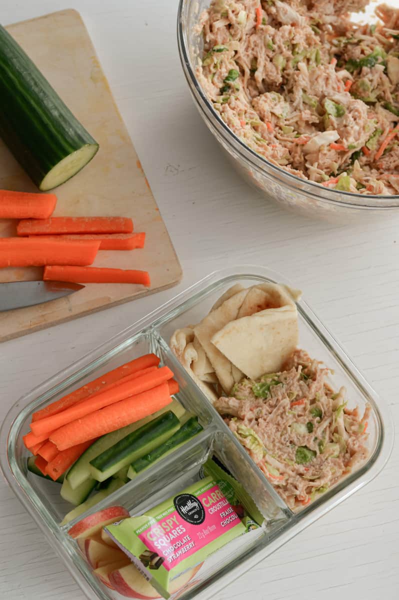 Adult lunchable with chicken salad, granola bar, apple slices and veggie slices.
