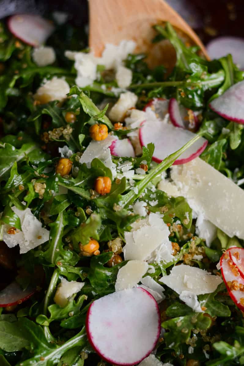Mixing arugula quinoa salad and topping with parmesan.