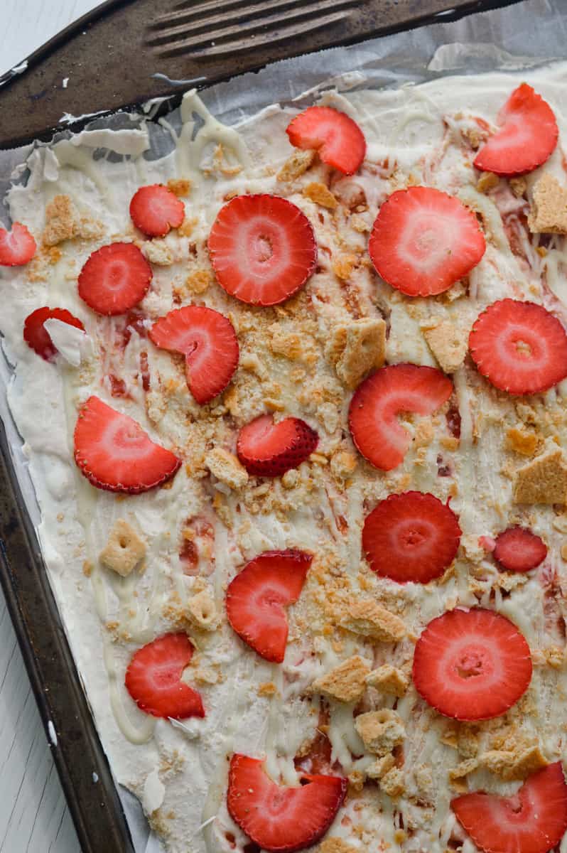 Adding graham crackers and strawberries to yogurt bark,