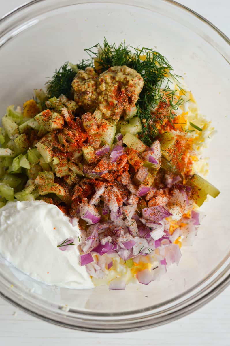 Adding egg salad ingredients to a bowl.