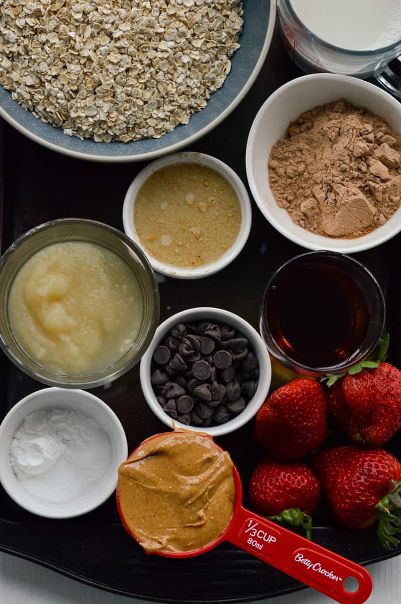 Ingredients for baked oats including oats, peanut butter, cocoa powder, applesauce and maple syrup.