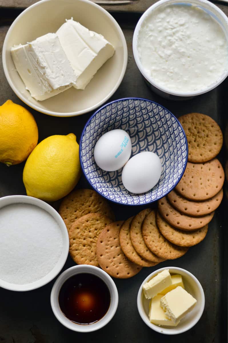 Ingredients for cheesecake including cream cheese, eggs, cottage cheese, lemon and digestive cookies.