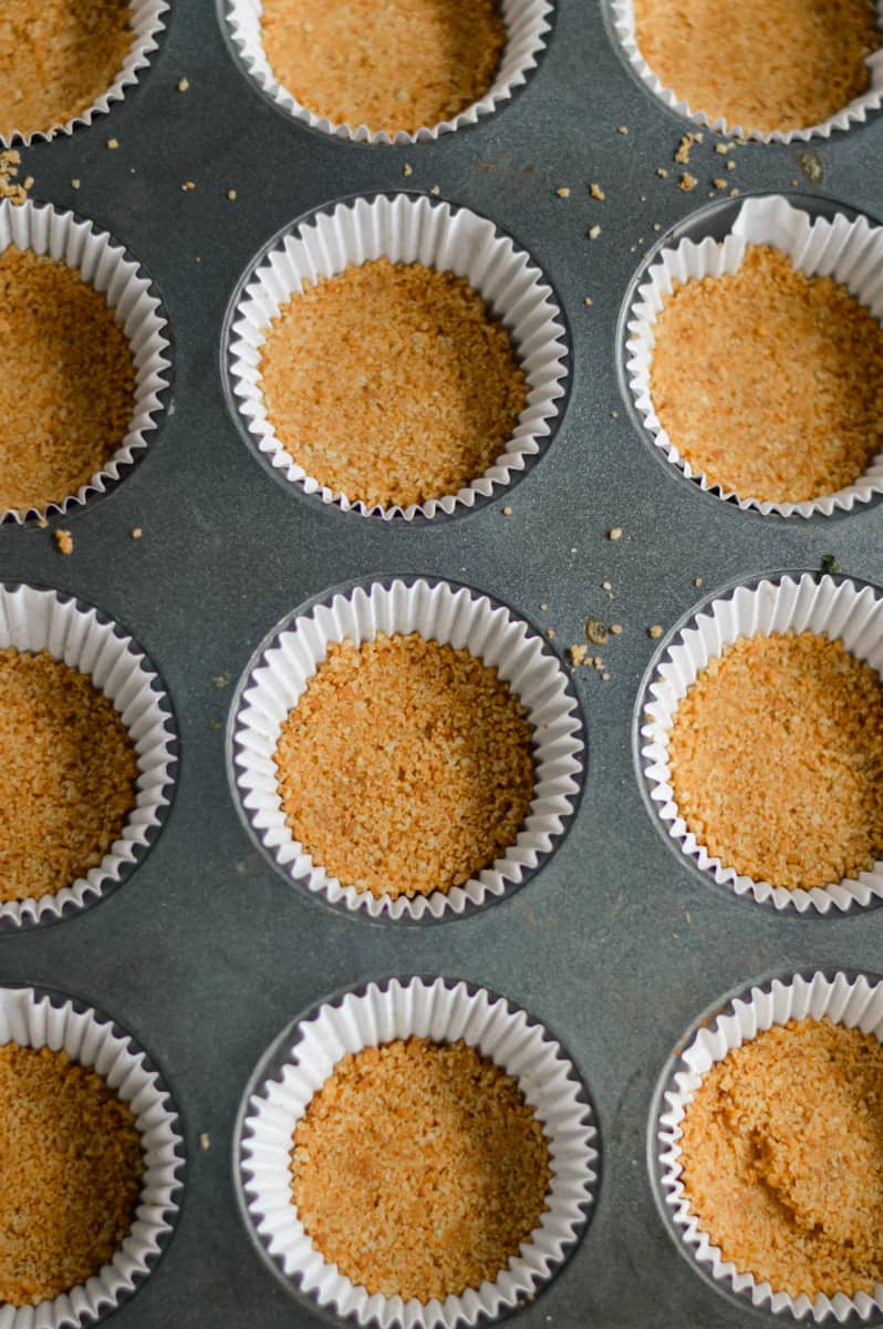 Pressing cheesecake crumb base into muffin liners.