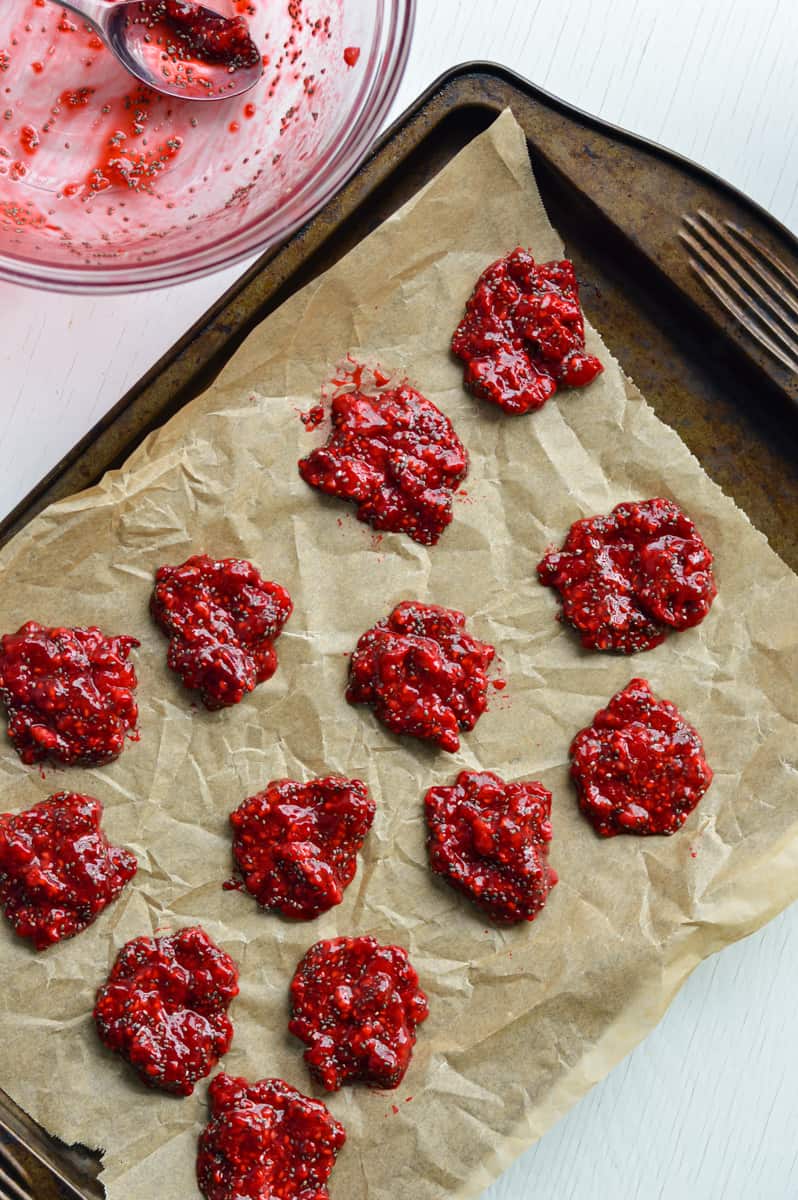 Spreading raspberry jam on lined sheet pan.