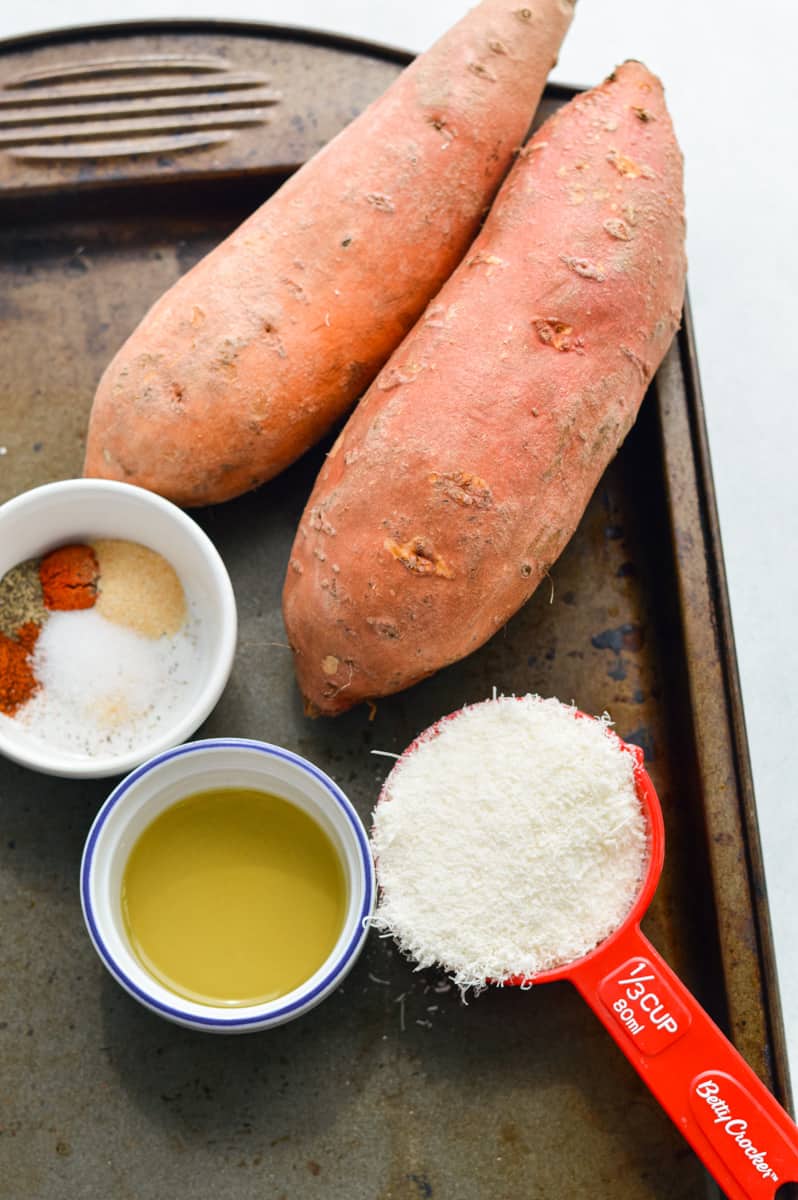 Ingredients on a tray including sweet potatoes, parmesan, olive oil and spices.