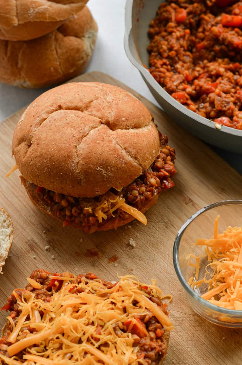 Assembling vegan sloppy joes with vegan cheese and hamburger buns.