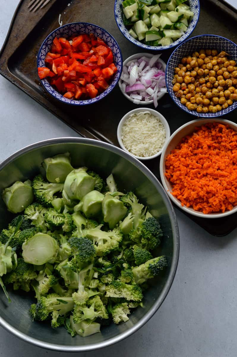 Ingredients including broccoli, cucumbers, peppers, onion, carrot, chickpeas and cheddar.