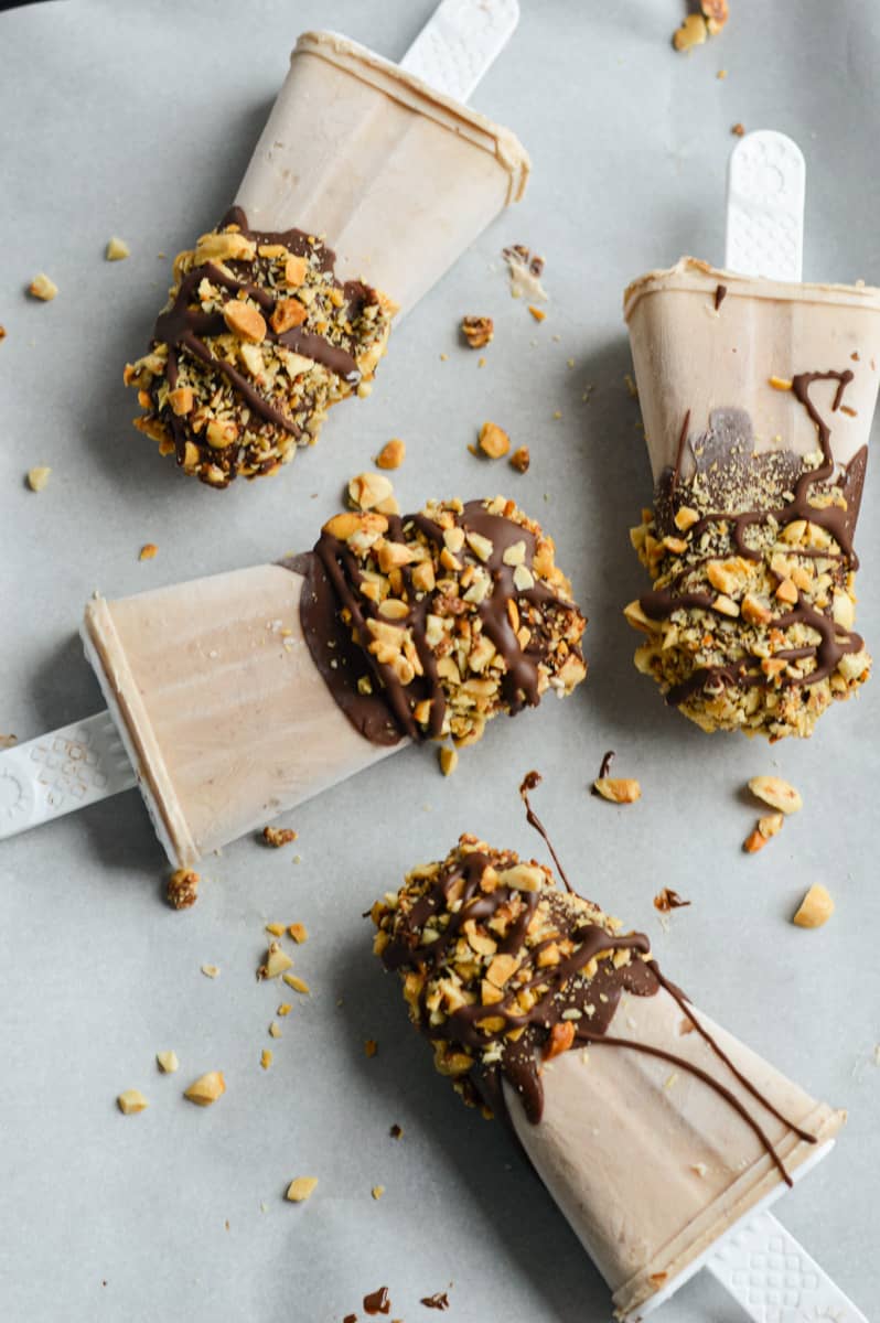 Four frozen yogurt bars coated in chocolate and peanuts.